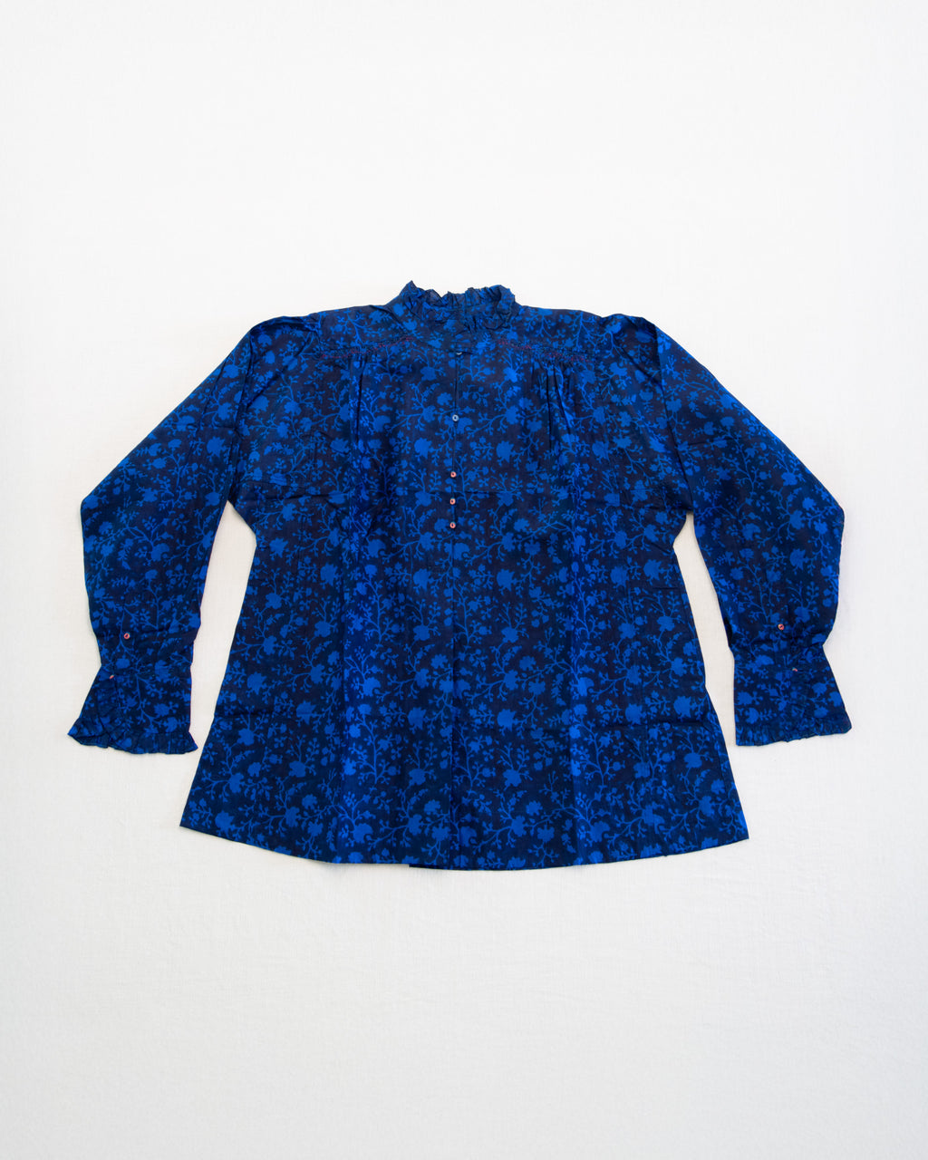 A blue floral silk top laid flat on a white background