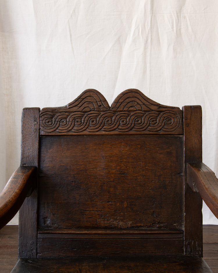 Wooden chair with intricate carvings against a white curtain background