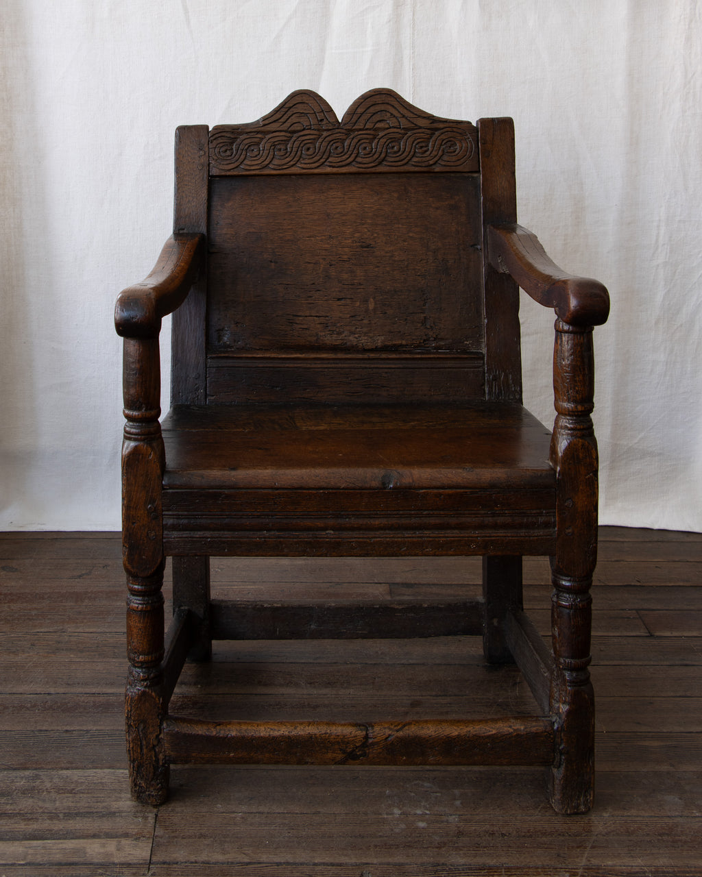 Antique wooden chair with intricate carvings on a wooden floor and white curtain background